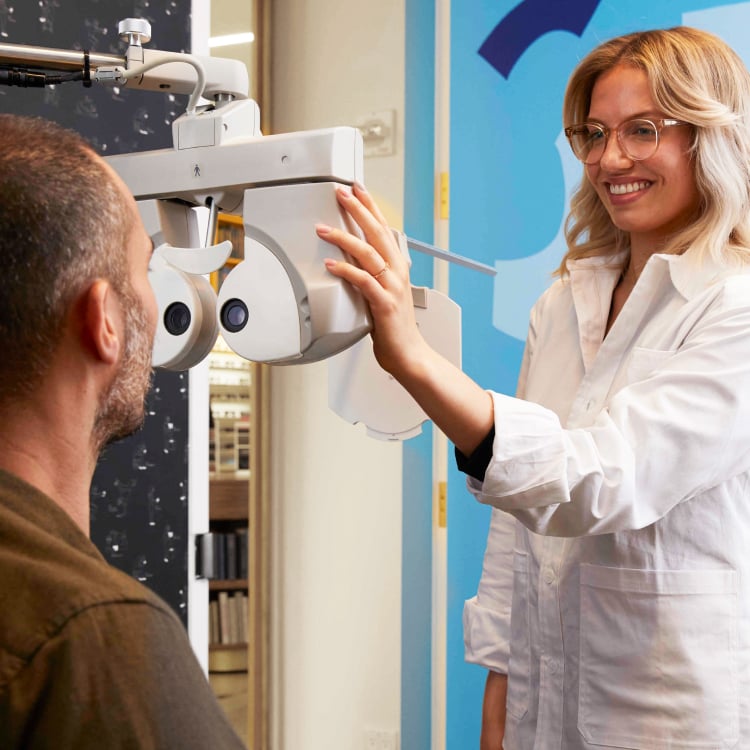 Smiling optometrist setting up a phoropter in front of a patient