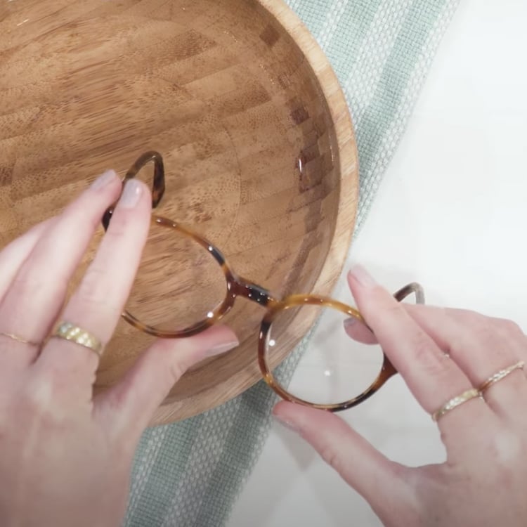 Hands holding glasses frames above a bowl of water