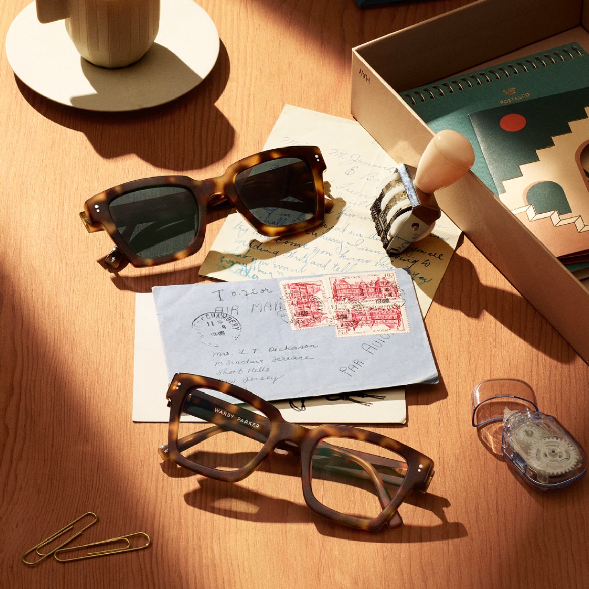 A pair of glasses and a pair of sunglasses on a table with international mail